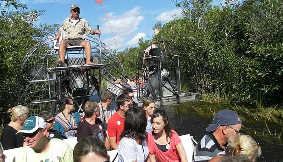 A group of people is enjoying an airboat tour through a wetland area with lush vegetation under a clear sky.