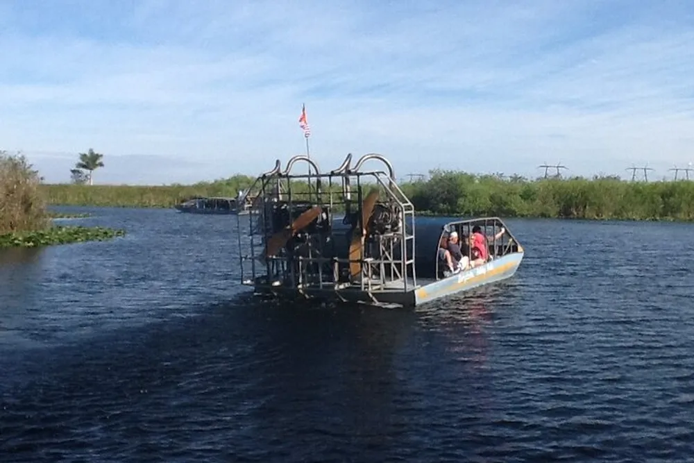 An airboat carrying passengers is gliding across a body of water likely in a wetland or marshy area