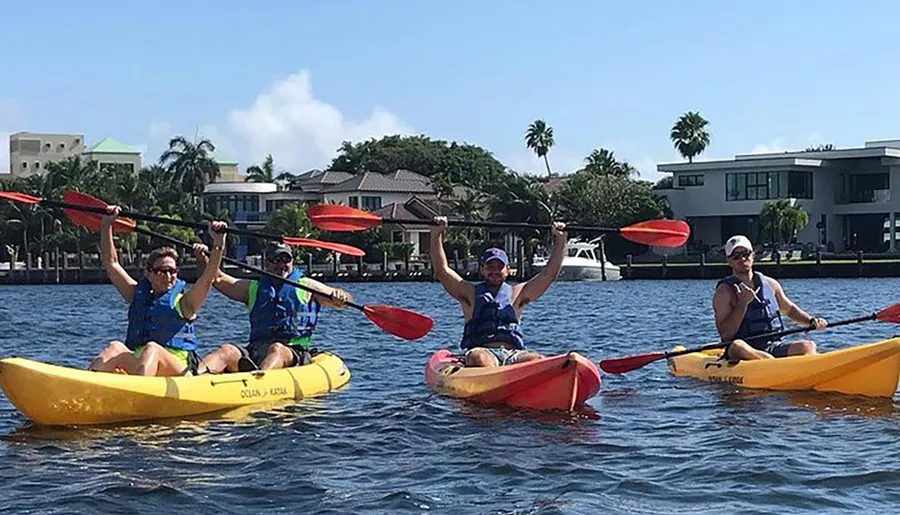 A group of four people are enjoying kayaking together on a sunny day in a calm waterway with houses in the background.