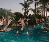 A group of people are enjoying a lively pool party at dusk with several individuals jumping into the water