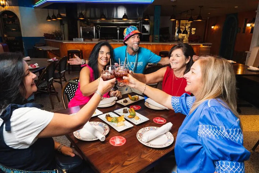A group of people are cheerfully toasting with drinks over a table with food in a restaurant setting