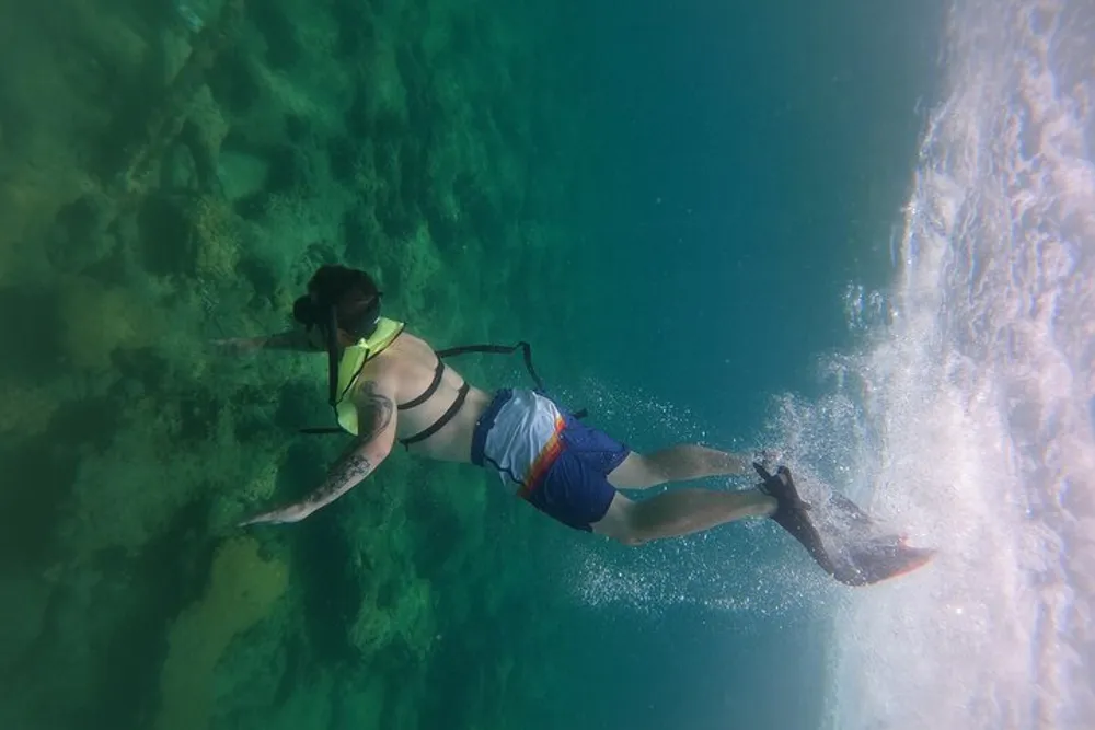 A person is free diving near the surface of a clear greenish aquatic environment creating a trail of bubbles