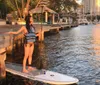 A person is standing atop a paddleboard close to a dock enjoying a sunny waterside scenery during golden hour