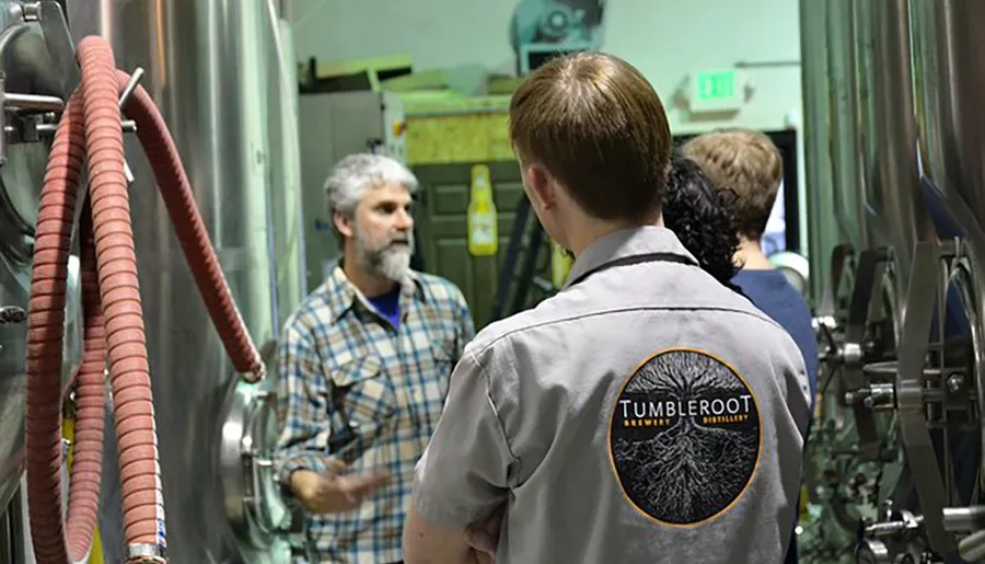 People are engaged in a discussion or tour inside a brewery called Tumbleroot, as indicated by the logo on the back of a person's shirt.