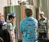 A group of people is touring a brewery learning about the beer production process among stainless steel fermentation tanks