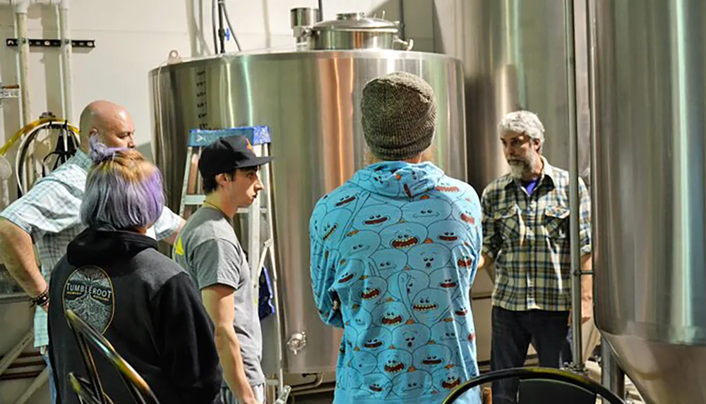 A group of people is touring a brewery learning about the beer production process among stainless steel fermentation tanks