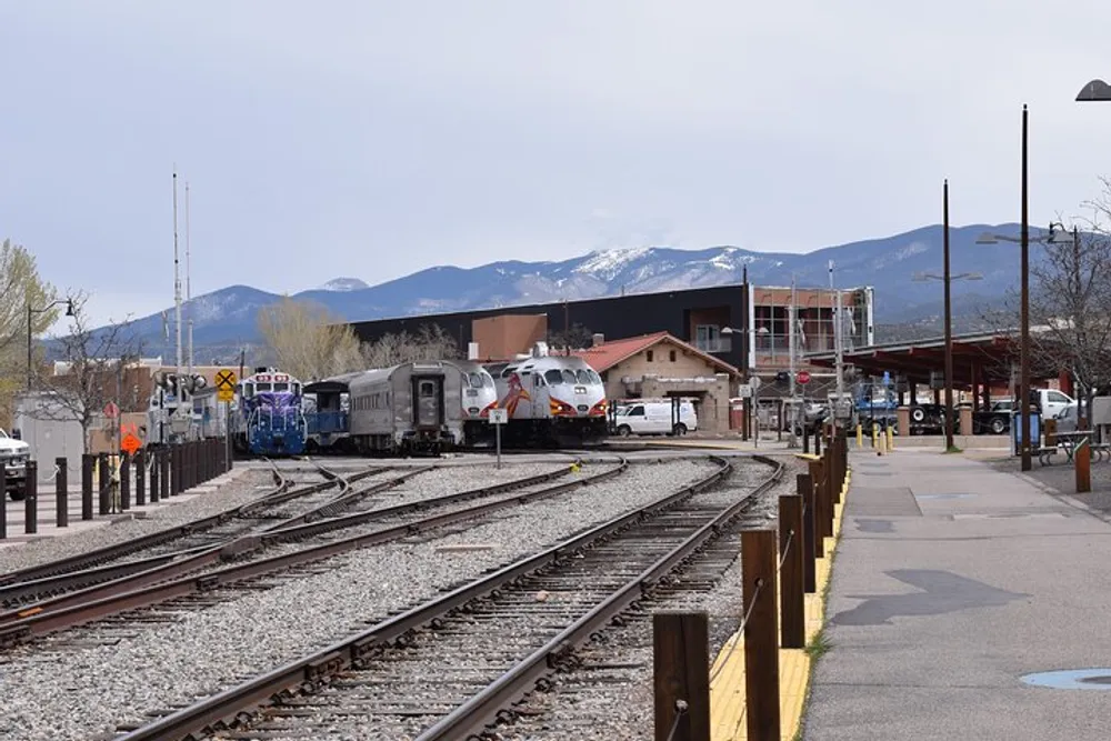A train station with multiple railway tracks where two trains are parked set against a backdrop of mountains with snow-capped peaks