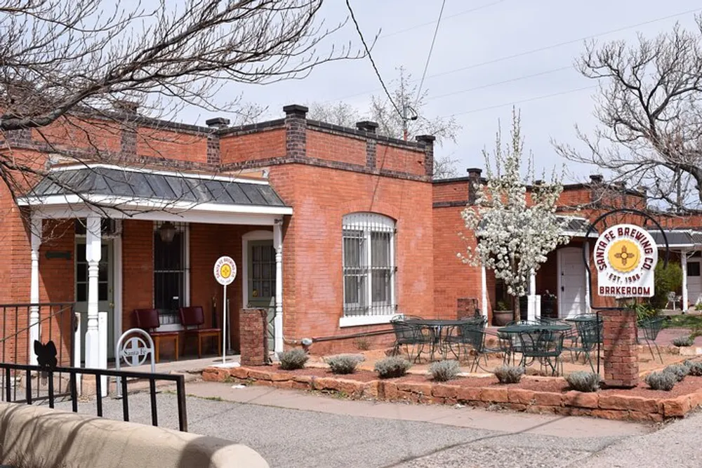 This image shows a quaint red brick building with a sign for State 48 Brewery Taproom adjacent to an outdoor seating area with wrought iron tables and chairs amidst a residential street