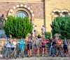 A group of people wearing helmets poses with their bicycles in front of a historic building and a statue
