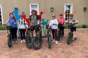 A group of people wearing matching orange flame-themed helmets are posing with their bicycles, smiling for a photo in a courtyard.