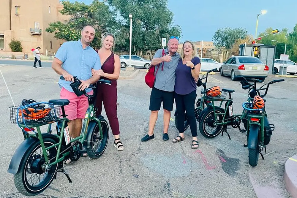 Four happy people are posing for a photo with electric bikes on a city street at twilight