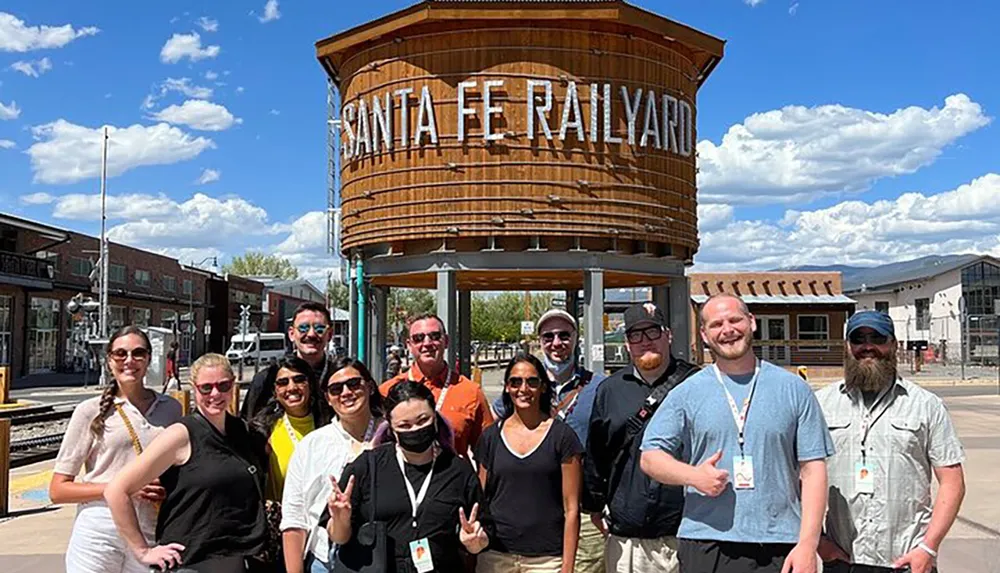A diverse group of people is posing for a photo at the Santa Fe Railyard with a clear sky in the background