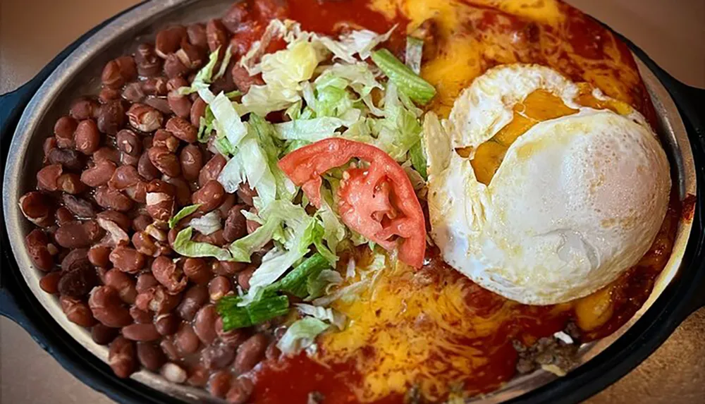 The image shows a colorful Mexican dish featuring sunny-side-up eggs on top of saucy enchiladas served with a side of beans and garnished with lettuce and tomato
