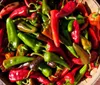 A basket is filled with a variety of vibrant green and red chili peppers basking in the sunlight