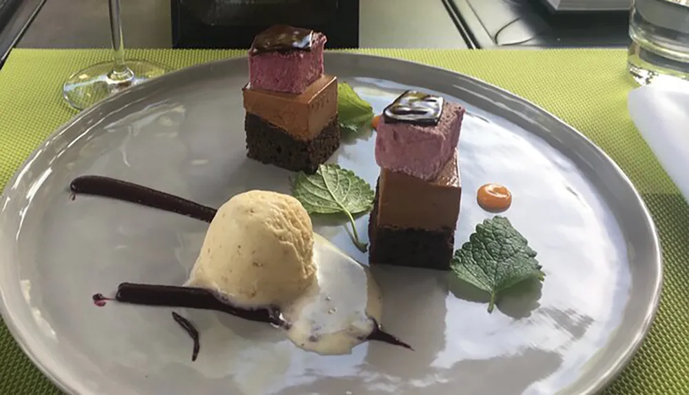 An elegantly plated dessert featuring layers of chocolate cake and mousse accompanied by a scoop of vanilla ice cream and decorative foliage on a white plate