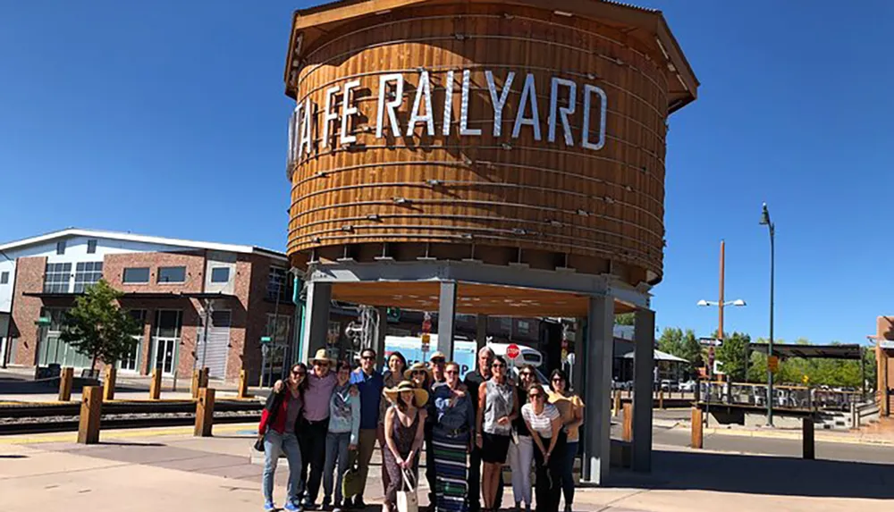 A group of people is posing for a photo in front of a large cylindrical structure with the words THE RAILYARD on it suggesting they are at a historical or renovated train station area that has been repurposed