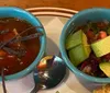 The image shows two bowls containing soup and a fresh salad with a spoon on the side