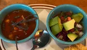The image shows two bowls containing soup and a fresh salad, with a spoon on the side.