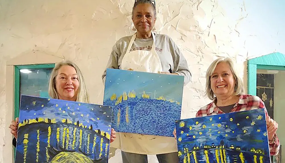 Three people are smiling and proudly displaying their paintings of a nightscape with reflections on water
