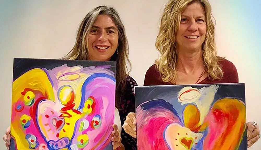 Two people are holding vibrant abstract paintings with heart shapes as the central theme