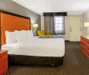 The image shows a neatly arranged hotel room with a large bed contemporary furniture and a warm color scheme