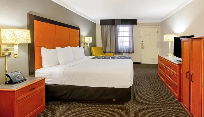 The image shows a neatly arranged hotel room with a large bed contemporary furniture and a warm color scheme