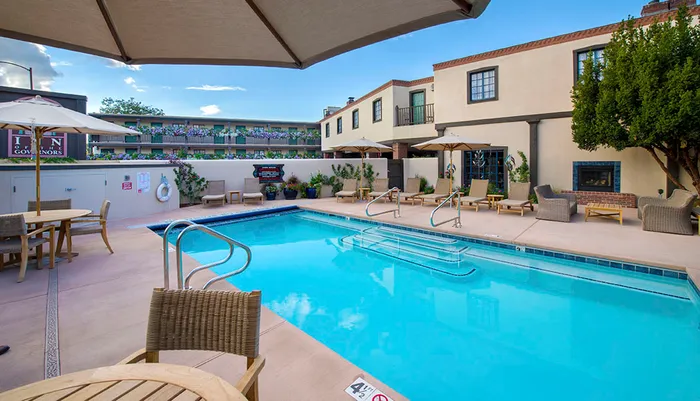 The image shows a serene outdoor hotel pool area flanked by loungers and umbrellas with a fireplace and a building backdrop labeled INN OF THE GOVERNORS