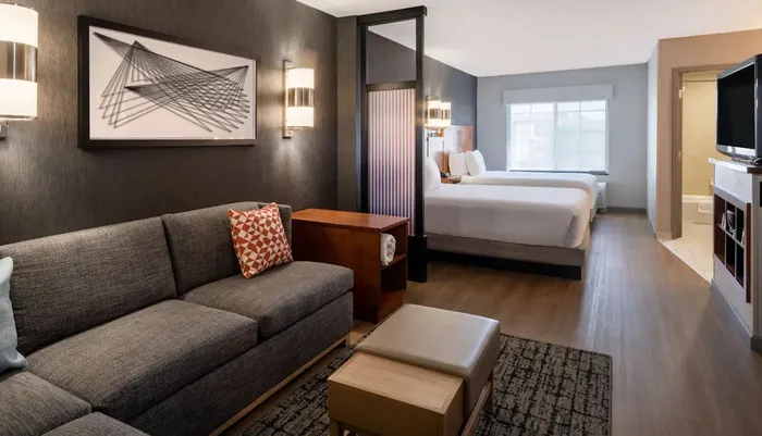 The image displays a modern hotel suite with a separate living area and bedroom characterized by contemporary furniture warm lighting and tasteful decor