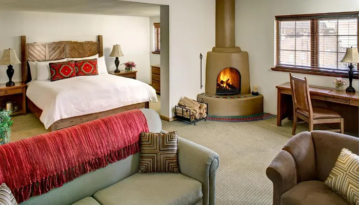 The image shows a cozy and well-appointed bedroom with a lit fireplace a comfortable seating area and Southwestern-style dcor accents
