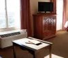The image shows a neatly arranged hotel room with a large bed side tables with lamps a window with curtains and a desk area with a television