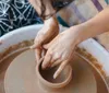 A person is shaping clay on a pottery wheel their hands and the wheel covered in wet clay