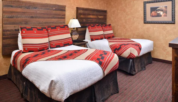 The image shows a hotel room with two beds adorned with southwestern-style red and beige bedding wood headboards and a wall painting complementing the rooms rustic decor theme