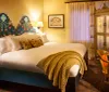 This image features a warmly lit cozy hotel room with a large bed adorned with colorful headboard designs decorative pillows and a draped throw blanket complemented by vintage-style furniture and a classical ambiance
