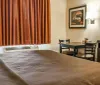 The image shows a neatly arranged hotel room with two double beds a bedside lamp and a warm color scheme
