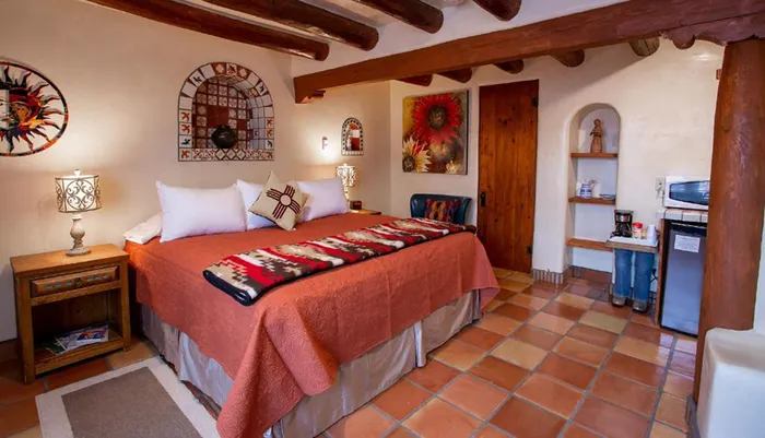 The image shows a cozy southwestern-styled room with terracotta floor tiles a rustic wooden beam ceiling and culturally-inspired decor and textiles