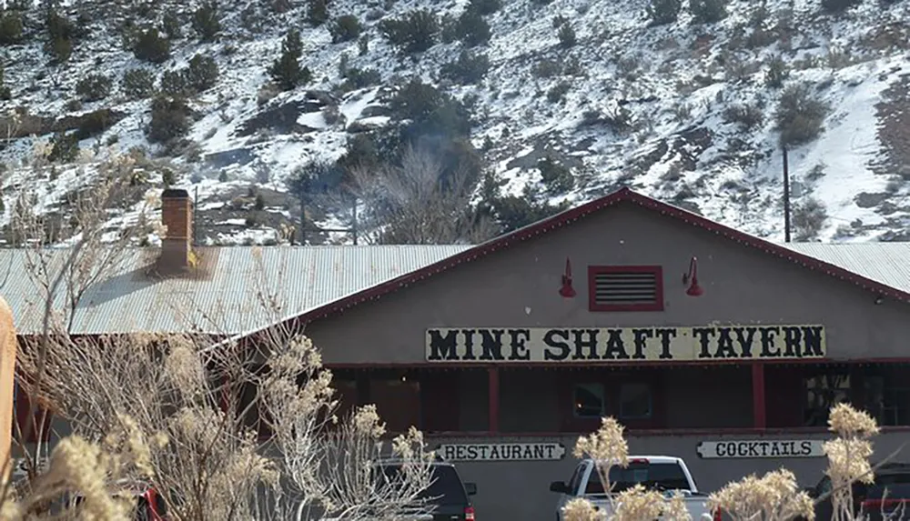 The Mine Shaft Tavern appears as a rustic restaurant and bar nestled in a snowy mountainous landscape