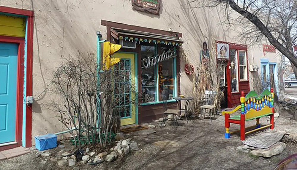 The image shows a quaint and colorful storefront with the word Chocolate displayed on the window accompanied by outdoor seating and vibrant artistic decorations
