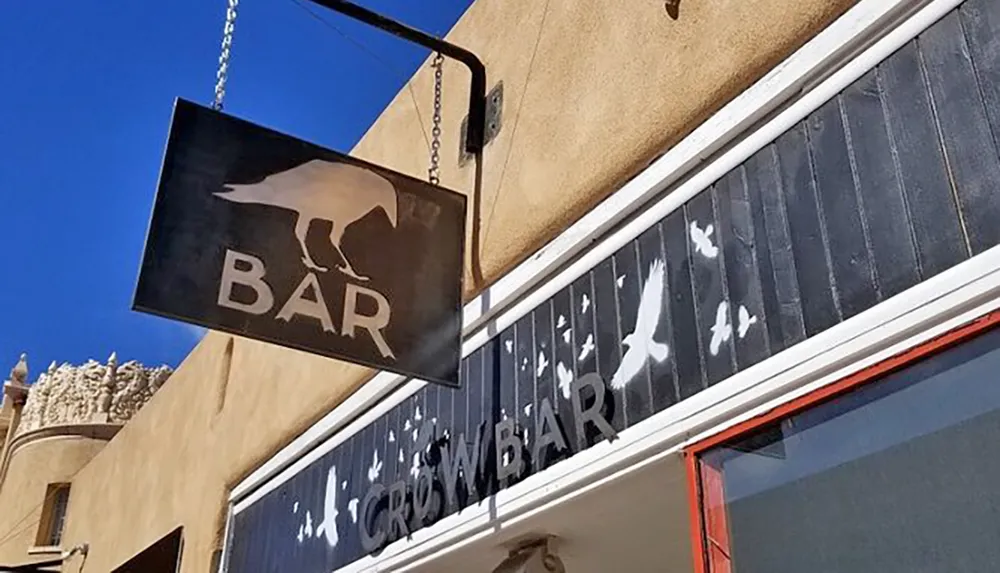 The image shows an exterior view of a bar with a crow-themed sign and decorative bird silhouettes on the buildings facade