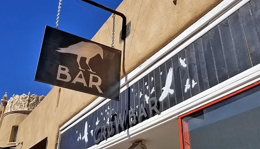 The image shows an exterior view of a bar with a crow-themed sign and decorative bird silhouettes on the building's facade.