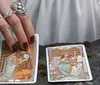 A hand adorned with rings touches a tarot card laid on a surface among other scattered cards
