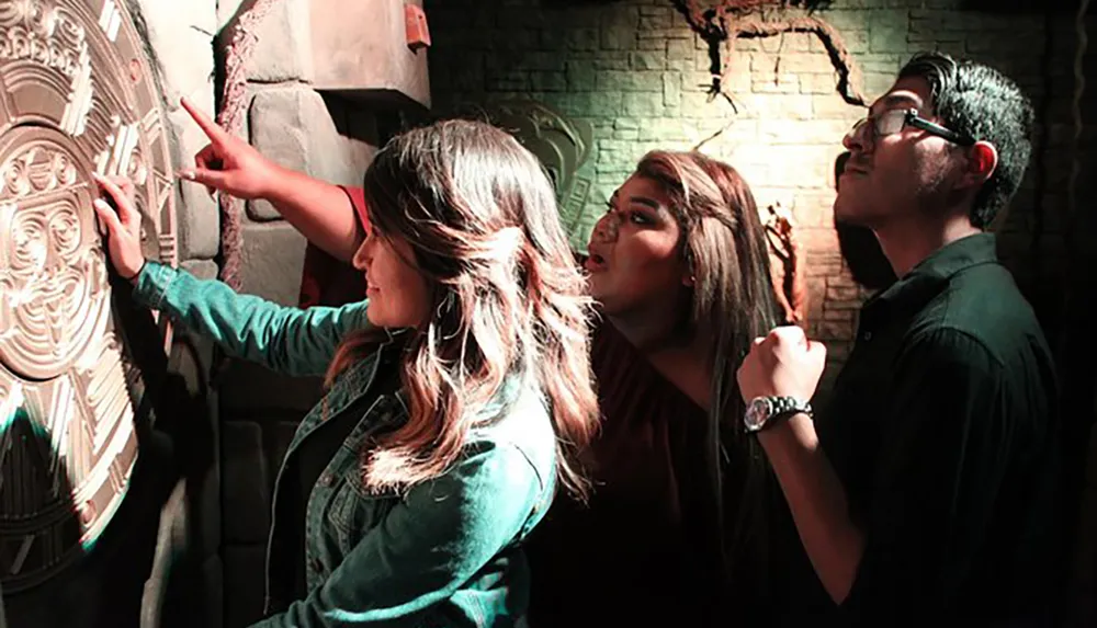 Three people are interacting with a wall-mounted decorative round object in a room with a brick-like texture and ambient lighting