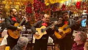 Three mariachi musicians are performing in a festive and decorated restaurant while patrons listen.