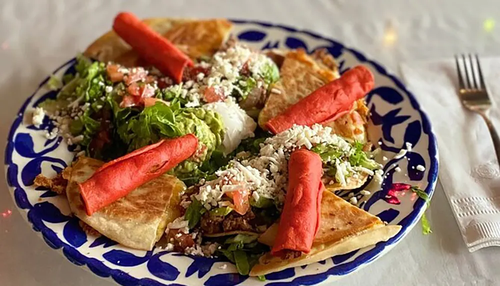 The image shows a variety of Mexican food items including red taquitos and quesadillas garnished with lettuce guacamole tomato and crumbled cheese on a decorative plate