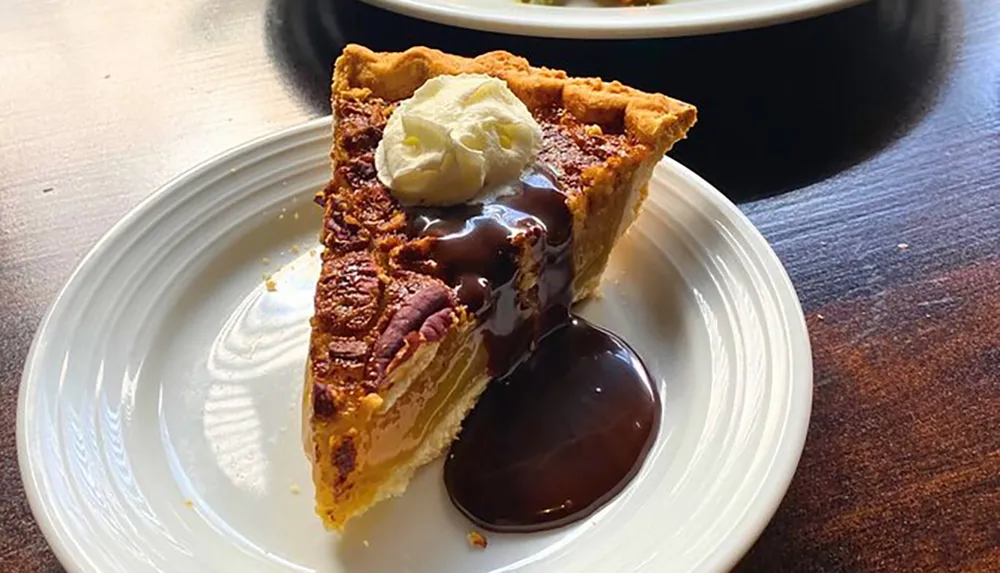 A slice of pecan pie is served with a dollop of whipped cream and a drizzle of chocolate sauce on a white plate