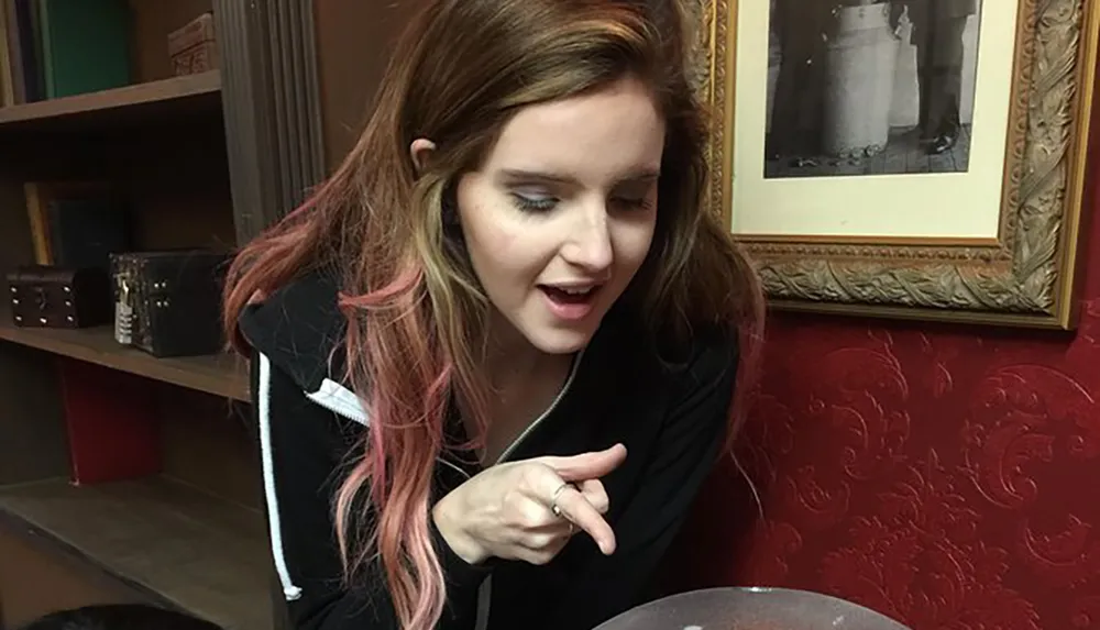 A person looks surprised or intrigued while pointing at something off-camera sitting in a room with a red wall and framed picture in the background