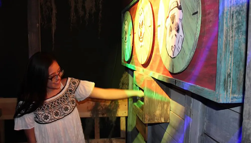 A smiling person is extending their arm towards colorful spinning illuminated wheels painted with animal faces at what appears to be an amusement park or carnival setting
