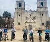 A group of people on electric bikes are posing for a photo in front of an old church with two bell towers