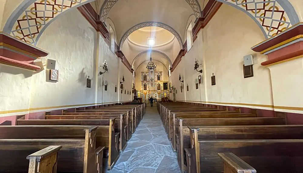 The image shows the interior of a church with wooden pews lining a central aisle leading to an altar featuring vaulted ceilings and decorative arches