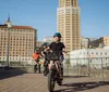 Three individuals are cycling along a path with a cityscape in the background