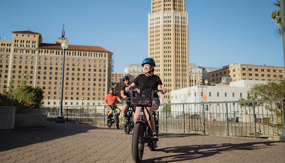 Three individuals are cycling along a path with a cityscape in the background